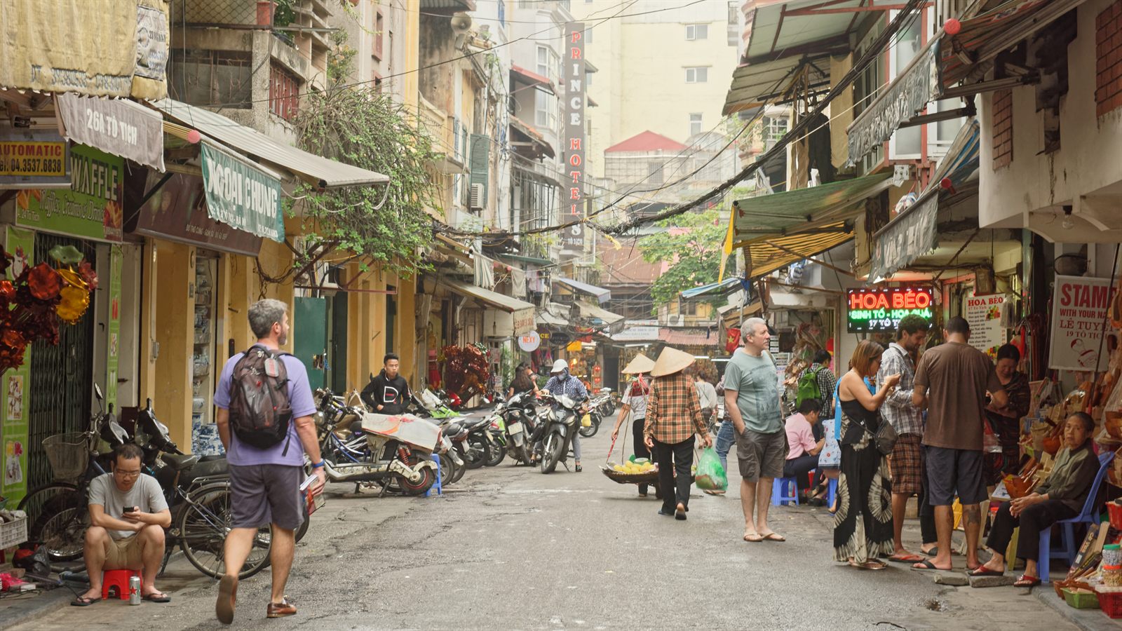 Backpackers, food stalls and parked scooters on a busy Hanoi old-quarter street, the kind of trip new advisors learn to plan in travel agent training for beginners