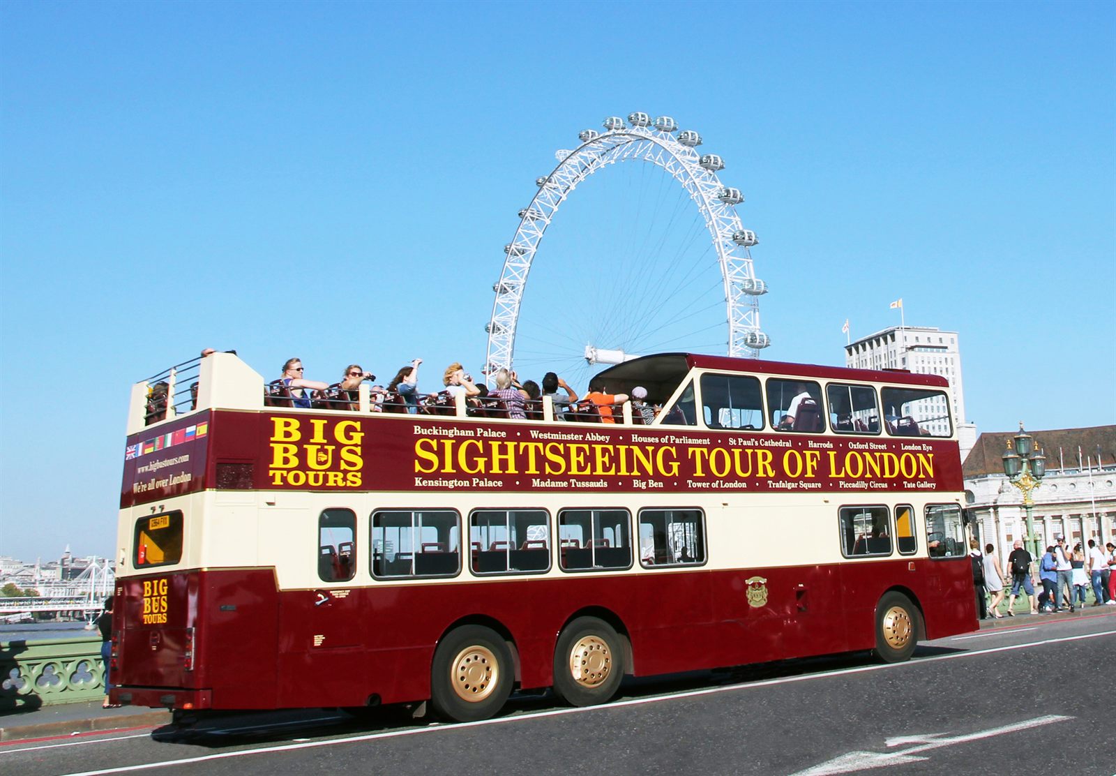 Red open-top sightseeing bus full of visitors passing the London Eye, the kind of product travel agent training teaches advisors to sell